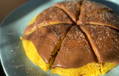 Fotografia mostra mini bolo de cenoura dourado e úmido, coberto com calda cremosa de chocolate brilhante e lascas de chocolate ralado no topo.