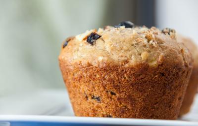 Fotografia em tons claros de um muffin de passas e aveia sobre um apoio branco.