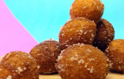 Fotografia de vários bolinhos doces fritos passados no açúcar e canela. Os bolinhos estão juntos, sobre uma tábua de madeira, com um fundo rosa e azul claro forte. Fotografia de vários bolinhos doces fritos passados no açúcar e canela. Os bolinhos estão juntos, sobre uma tábua de madeira, com um fundo rosa e azul claro forte.