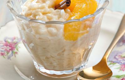 fotografia em tons de branco e amarelo tirada de um prato redondo branco com um copo transparente que contém arroz doce com rodelas de laranja de canela fotografia em tons de branco e amarelo tirada de um prato redondo branco com um copo transparente que contém arroz doce com rodelas de laranja de canela
