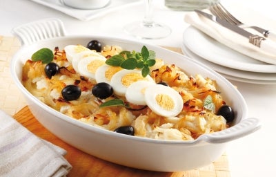 Em cima de uma mesa, refratário com bacalhau, cebola, ovos cortados em rodelas e azeitonas pretas, decorado com folhas de manjericão. Em cima de uma mesa, refratário com bacalhau, cebola, ovos cortados em rodelas e azeitonas pretas, decorado com folhas de manjericão.