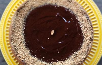 Foto da receita de Torta de Amendoim. Observa-se uma torta com ganache e farofa de amendoim em cima sobre um prato de amendoim. Foto da receita de Torta de Amendoim. Observa-se uma torta com ganache e farofa de amendoim em cima sobre um prato de amendoim.