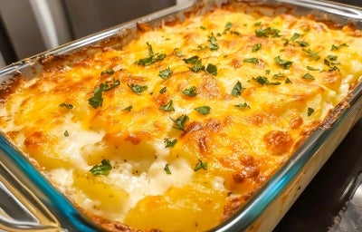 Em cima de uma mesa, refratário com batatas com queijo gratinado, decorado com cheiro-verde picado.