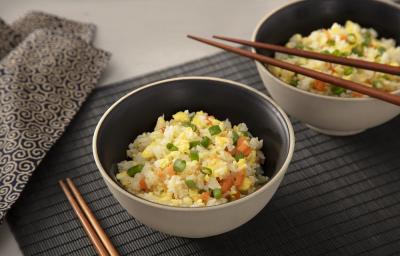 Foto da receita de yakimeshi. Observa-se duas tigelas com o arroz dentro sobre uma esteira preta e dois hashis apoiados.