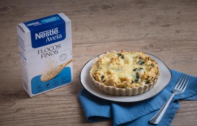Foto da receita de quiche de aveia com espinafre servida em um grande prato desforme branco sobre um pano azul em cima de uma mesa de madeira Foto da receita de quiche de aveia com espinafre servida em um grande prato desforme branco sobre um pano azul em cima de uma mesa de madeira