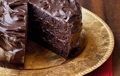 Fotografia de um bolo marrom de chocolate com uma fatia faltando, em um prato dourado em cima de um guardanapo de tecido vermelho em uma mesa de madeira escura. Fotografia de um bolo marrom de chocolate com uma fatia faltando, em um prato dourado em cima de um guardanapo de tecido vermelho em uma mesa de madeira escura.