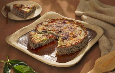 Foto da receita de quiche de aveia corte rústico servido em uma porção com uma fatia cortada sobre uma base quadrada de cerãmica marrom com um pano de linho bege ao lado