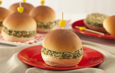 A foto contém diversos pães com hamburguês e palitos com uma bolinha amarela por cima. Um prato vermelho com um pão com hambúrguer à frente A foto contém diversos pães com hamburguês e palitos com uma bolinha amarela por cima. Um prato vermelho com um pão com hambúrguer à frente