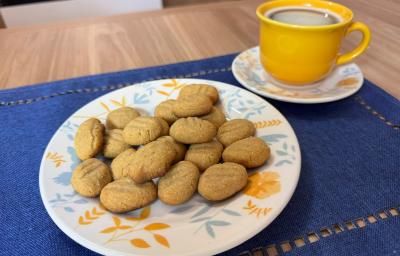 Fotografia de um pano retangular azul sobre uma mesa de madeira. Sobre o pano tem um prato branco com desenhos em tom pastel de cor azul e laranja, dentro do prato tem alguns biscoitos de farinhas láctea. Ao lado do prato tem uma xícara amarela. Fotografia de um pano retangular azul sobre uma mesa de madeira. Sobre o pano tem um prato branco com desenhos em tom pastel de cor azul e laranja, dentro do prato tem alguns biscoitos de farinhas láctea. Ao lado do prato tem uma xícara amarela.