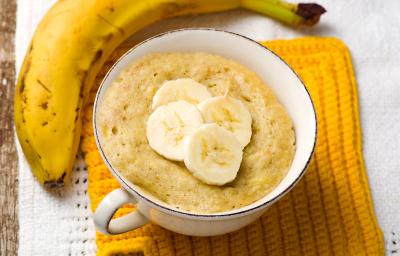 Fotografia em tons de amarelo com uma xícara de café ao centro. Dentro da xícara existe uma receita de bolo de banana. Ao lado existe uma banana inteira em cima de um pano amarelo Fotografia em tons de amarelo com uma xícara de café ao centro. Dentro da xícara existe uma receita de bolo de banana. Ao lado existe uma banana inteira em cima de um pano amarelo