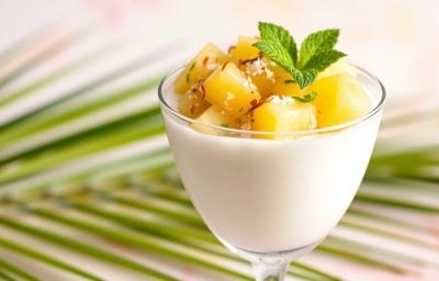 Fotografia em tons claros de uma taça de vidro com o creme de abacaxi e cubos de abacaxi mais caramelizados com folhas de hortelã por cima.