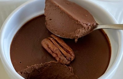Fotografia de alguns ramkins brancos com mousse de chocolate. O mousse do centro da foto tem uma castanha decorando e uma colher tirando a porção da mousse. Fotografia de alguns ramkins brancos com mousse de chocolate. O mousse do centro da foto tem uma castanha decorando e uma colher tirando a porção da mousse.