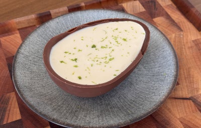 imagem mostra um ovo de páscoa de chocolate escuro recheado de um creme branco por cima e raspas de limão verdes