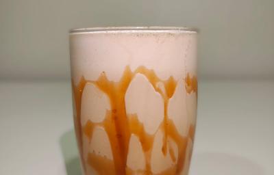 Foto da receita de nescafé caramelo gelado servida no copo de vidro alto sobre uma mesa branca