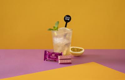 Foto da receita de Soda Italiana Passion Fruit and Lemon. Observa-se um fundo amarelo e roxo com um copo alto no centro, cheio de gelo, com uma rodela de limão siciliano. Meio maracujá decora a foto à direita, assim como folhas de hortelã no copo. Foto da receita de Soda Italiana Passion Fruit and Lemon. Observa-se um fundo amarelo e roxo com um copo alto no centro, cheio de gelo, com uma rodela de limão siciliano. Meio maracujá decora a foto à direita, assim como folhas de hortelã no copo.