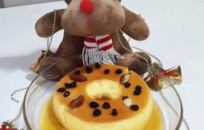 Foto da Receita de Pudim de Leite Moça Com Amêndoas e Passas. Observa-se um pudim em uma travessa redonda de vidro e festivo, decorado com uma rena de Natal!