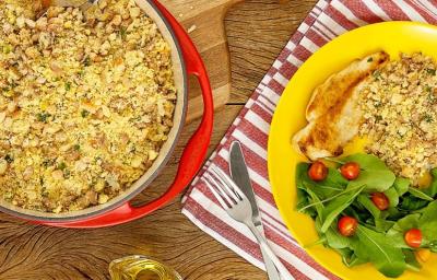 Fotografia em tons de amarelo e vermelho em uma bancada de madeira com um pano vermelho listrado com um prato amarelo com salada verde, arroz, frango e farofa de feijão. Ao lado, uma frigideira vermelha com farofa dentro. Fotografia em tons de amarelo e vermelho em uma bancada de madeira com um pano vermelho listrado com um prato amarelo com salada verde, arroz, frango e farofa de feijão. Ao lado, uma frigideira vermelha com farofa dentro.