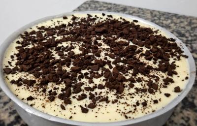 Fotografia de uma forma de alumínio redonda e grande com uma receita de pavê delícia de limão com kitkat branco e negresco por cima.