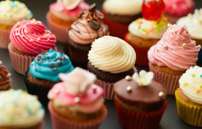 Fotografia de várias unidades de forminhas com cupcakes diversos coloridos e confeitados sobre uma mesa preta.