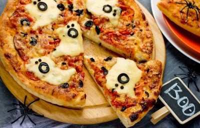 Pizza com massa dourada, fantasmas de queijo, olhos de azeitona preta e borda crocante, pronta para servir no Halloween.