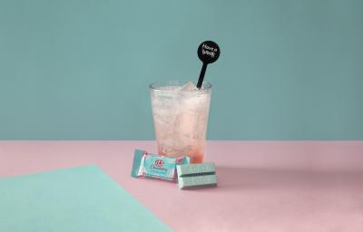 Foto da receita de Soda Italiana Bubble Gum. Observa-se um fundo azul bebê com o copo alto ao centro, com xarope de chiclete e servido com KIT KAT Cotton Candy