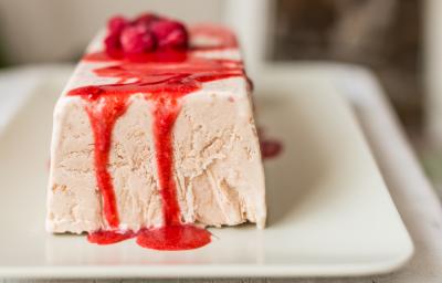 Fotografia de uma terrine de iogurte, em formato de uma forma retangular. Por cima, uma calda de frutas vermelhas, sobre um prato branco quadrangular. Fotografia de uma terrine de iogurte, em formato de uma forma retangular. Por cima, uma calda de frutas vermelhas, sobre um prato branco quadrangular.