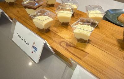 Fotografia em tons de marrom com uma bancada de madeira ao centro. Em cima da bancada existem pequenos potes de sobremesa com uma camada de biscoitos e uma camada de creme branco. A frente desses copos existe uma escrito "Torta de Limão" Fotografia em tons de marrom com uma bancada de madeira ao centro. Em cima da bancada existem pequenos potes de sobremesa com uma camada de biscoitos e uma camada de creme branco. A frente desses copos existe uma escrito "Torta de Limão"