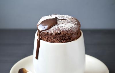 Fotografia de um suflê de café com NESCAFÉ e açúcar de confeiteiro polvilhado por cima. A sobremesa está em um recipiente de vidro branco alto em cima de um prato pequeno branco de sobremesa, e uma colher de café apoiada. Fotografia de um suflê de café com NESCAFÉ e açúcar de confeiteiro polvilhado por cima. A sobremesa está em um recipiente de vidro branco alto em cima de um prato pequeno branco de sobremesa, e uma colher de café apoiada.