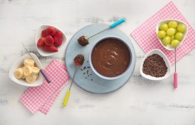 fotografia em tons de rosa e cinza de uma bancada vista de cima, ao centro panos listrados na cor rosa e branco, uma mini tabua azul com um recipiente redondo em cima com chocolate, 4 potes brancos um com granulado e os demais com frutas. fotografia em tons de rosa e cinza de uma bancada vista de cima, ao centro panos listrados na cor rosa e branco, uma mini tabua azul com um recipiente redondo em cima com chocolate, 4 potes brancos um com granulado e os demais com frutas.