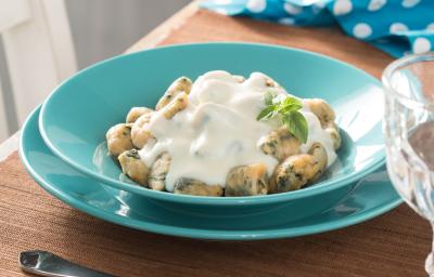 Fotografia em tons de azul em uma bancada de madeira, um paninho azul com bolinhas brancas, prato redondo verde com o nhoque nutritivo com molho branco. Fotografia em tons de azul em uma bancada de madeira, um paninho azul com bolinhas brancas, prato redondo verde com o nhoque nutritivo com molho branco.