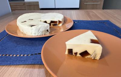 Fotografia de dois pratos rasos de tom marrom claro apoiados em uma mesa de madeira com um pano azul quadrado. Sobre o prato da frente tem uma fatia grande de gelatina cremosa de leite moça com cubinhos de gelatina de café. No outro tem o restante. Fotografia de dois pratos rasos de tom marrom claro apoiados em uma mesa de madeira com um pano azul quadrado. Sobre o prato da frente tem uma fatia grande de gelatina cremosa de leite moça com cubinhos de gelatina de café. No outro tem o restante.
