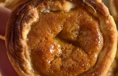 Fotografia de uma mão segurando um pastel de nata no centro da foto. No fundo, atrás do pastel, tem mais unidades. Fotografia de uma mão segurando um pastel de nata no centro da foto. No fundo, atrás do pastel, tem mais unidades.