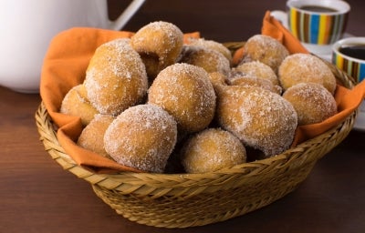 Em cima de uma mesa, cesta de palha com pano laranja com bolinhos de chuva, polvilhado com açúcar de confeiteiro.