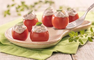 Foto em tons de verde da receita de tomatinho recheado servido em algumas porções em um prato exótico de madeira sobre um pano verde com algumas folhas de decoração Foto em tons de verde da receita de tomatinho recheado servido em algumas porções em um prato exótico de madeira sobre um pano verde com algumas folhas de decoração