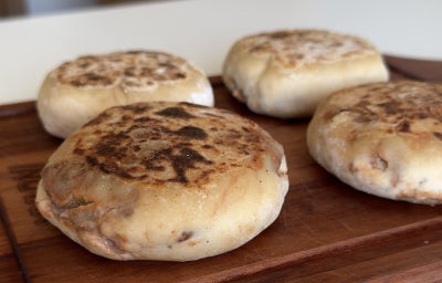 Fotografia mostra quatro salgados assados com textura crocante sobre uma tabua de madeira.