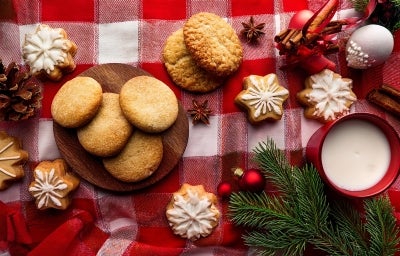 Em cima de uma mesa decorada de Natal, prato com biscoitos redondos e formado de estrelas crocantes, os em formato de estrela estão decorados com glacê branco.