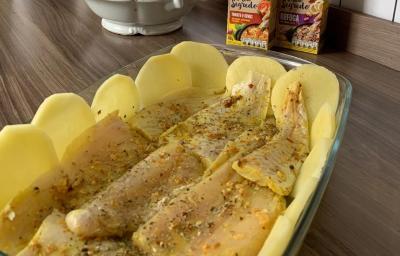 Foto aproximada da receita de Tilápia Assada com Batata no forno, servida em uma travessa de vidro em uma bancada com os temperos maggi meu segredo ao fundo Foto aproximada da receita de Tilápia Assada com Batata no forno, servida em uma travessa de vidro em uma bancada com os temperos maggi meu segredo ao fundo