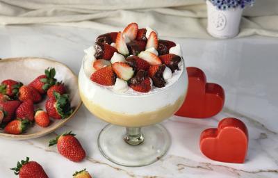 Foto da receita de Morangoffee na Taça, servida em uma grande taça de vidro, em duas camadas, uma de creme bege e outra de creme branco, decorada com morangos com chocolate e suspiros, em uma bancada com mais morangos e alguns corações decorativos Foto da receita de Morangoffee na Taça, servida em uma grande taça de vidro, em duas camadas, uma de creme bege e outra de creme branco, decorada com morangos com chocolate e suspiros, em uma bancada com mais morangos e alguns corações decorativos