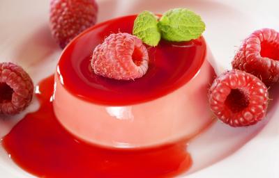 Fotografia em tons de rosa com uma gelatina de frutas vermelhas ao centro. Por cima da gelatina existe algumas framboesas e uma folha de hortelã Fotografia em tons de rosa com uma gelatina de frutas vermelhas ao centro. Por cima da gelatina existe algumas framboesas e uma folha de hortelã