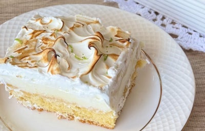 Foto aproximada de uma fatia da receita de Bolo Torta de Limão, com uma camada de bolo branco, outra de recheio e finalizado com merengue levemente maçaricado