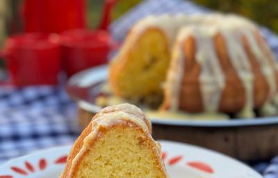Fotografia de um pedaço de bolo de laranja com brigadeiro de laranja em um prato raso branco grande. Ao fundo tem o restante do bolo com a calda. Fotografia de um pedaço de bolo de laranja com brigadeiro de laranja em um prato raso branco grande. Ao fundo tem o restante do bolo com a calda.