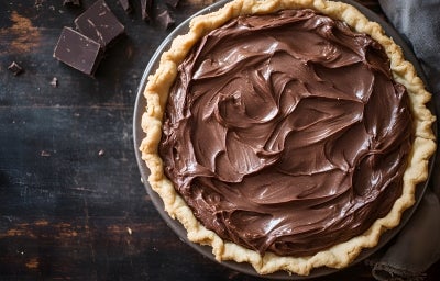 Fotografia vista de cima em tons escuros de uma torta com cobertura de chocolate sobre um praot grande e raso, apoiado em uma mesa de madeira escura.