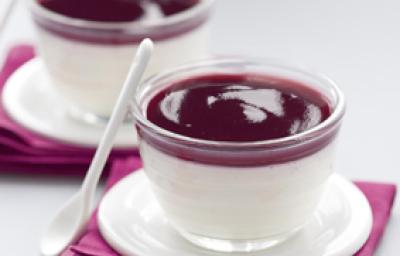 Fotografia em tons de roxo escuro em uma bancada de madeira cinza, dois guardanapos de pano roxos, dois pratinhos de café brancos e dois copinhos de vidro com a sobremesa pannacotta com calda de vinho tinto dentro. Fotografia em tons de roxo escuro em uma bancada de madeira cinza, dois guardanapos de pano roxos, dois pratinhos de café brancos e dois copinhos de vidro com a sobremesa pannacotta com calda de vinho tinto dentro.