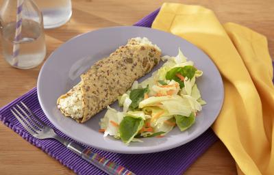Fotografia em tons de lilás com um prato lilás ao centro e uma toalha amarela. Dentro do prato existe uma receita de wrap com sementes de chia e abóbora recheado com um creme de ricota com Ninho e acompanhado de uma salada.