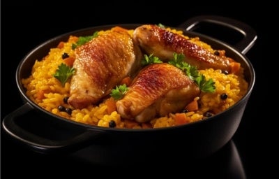 Panela preta com arroz cremoso amarelo com pedaços de cenoura, pedaços de frango e decorado com folhas de salsa.