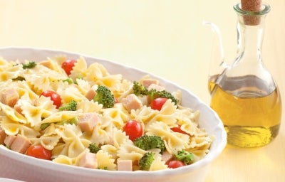 Travessa branca com salada de macarrão gravatinha com peito de peru, brócolis e tomate cereja com um vidro de azeite ao lado. Travessa branca com salada de macarrão gravatinha com peito de peru, brócolis e tomate cereja com um vidro de azeite ao lado.
