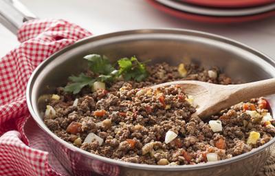 Fotografia em tons de vermelho em uma bancada de madeira com um pano quadriculado em vermelho com uma frigideira com carne moída suculenta. Fotografia em tons de vermelho em uma bancada de madeira com um pano quadriculado em vermelho com uma frigideira com carne moída suculenta.