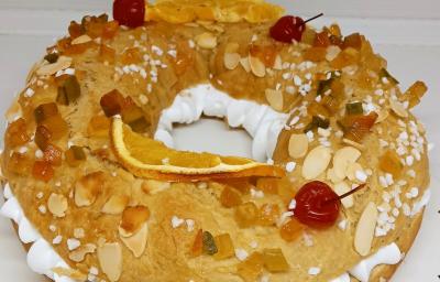 Foto da receita de Rosca de Reis. Observa-se uma rosca recheada com chantilly e decorada com frutas secas, cereja e amêndoas laminadas.