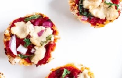 Fotografia em tons de vermelho em uma mesa branca, um prato redondo branco e vários pedaços pequenos de pizza feitas com massa de couve-flor e recheada de molho de tomate, rúcula e queijo mozarela. Fotografia em tons de vermelho em uma mesa branca, um prato redondo branco e vários pedaços pequenos de pizza feitas com massa de couve-flor e recheada de molho de tomate, rúcula e queijo mozarela.