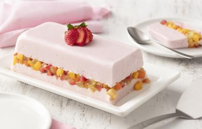 fundo de madeira branca com paninho rosa claro, um prato branco com uma camada de gelatina com iogurte de morango, uma camada de salada de frutas e mais uma camada de gelatina com iogurte de morango.